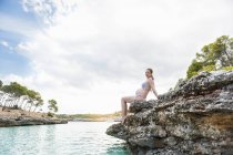 Schwangere sitzt auf Felsen am Meer — Stockfoto
