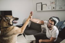 Jeune homme et chien haut cinq à l'intérieur — Photo de stock