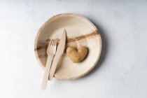 Patata a forma di cuore e forchetta e coltello in legno sul piatto di foglie di palma — Foto stock