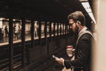 Молодий підприємець очікування на станції метро платформа, за допомогою смартфона — стокове фото