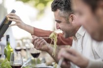 Мужчина ест спагетти возле семейного обеда в саду — стоковое фото