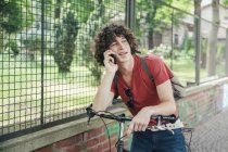 Giovane in piedi con la bicicletta al telefono — Foto stock