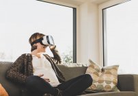 Pregnant woman on couch wearing VR glasses — Stock Photo