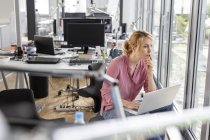 Frau mit Laptop im Büro schaut aus dem Fenster — Stockfoto