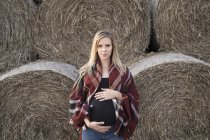 Smiling pregnant woman standing in front of bales of straw — Stock Photo