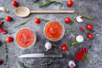 Two glasses of homemade tomato sauce and ingredients on stone surface — Stock Photo