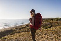 Teenage girl with backpack at seaside looking at distance in the evening twilight — Stock Photo