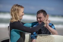 Heureux adolescent garçon avec le syndrome du duvet et femme avec planche de surf sur la plage — Photo de stock