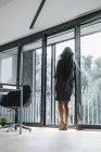 Donna con lunghi capelli grigi guardando fuori dalla finestra — Foto stock