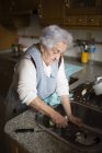 Old woman washing dishes in kitchen — Stock Photo