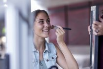 Glückliches junges Mädchen schminkt sich, während Mutter Spiegel hält — Stockfoto