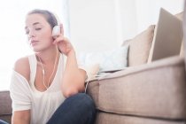 Young woman sitting on the floor of living room listening music with headphones — Stock Photo