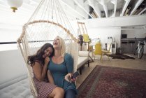 Две счастливые девушки в гамаке с сотовым телефоном — стоковое фото