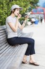 Женщина сидит на скамейке с помощью карманного зеркала для нанесения макияжа — стоковое фото