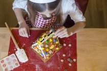 Mädchen schmückt Lebkuchenhaus am Schreibtisch — Stockfoto