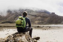 Турист с рюкзаком сидит на скале — стоковое фото