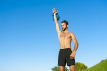 Man exercising with kettlebell under blue sky — Stock Photo