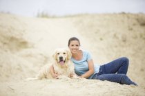 Sonriente joven con perro en la arena - foto de stock
