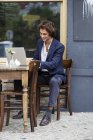 Smiling young businessman working with laptop at sidewalk cafe — Stock Photo