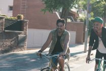 Due uomini sorridenti in bicicletta per strada in città nella giornata di sole — Foto stock