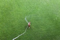 Petit garçon debout sur la pelouse et jouant avec tuyau d'arrosage — Photo de stock