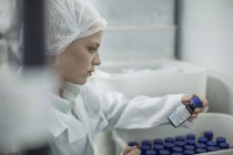 Laborangestellte in pharmazeutischer Fabrik schaut auf Tablettenflasche — Stockfoto