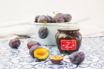 Preserving jar of homemade plum jam and plums on tiles — Stock Photo