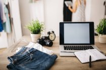 Laptop, clothes and sketchbook on desk with woman in background — Stock Photo