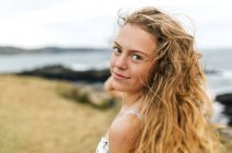 Porträt eines lächelnden blonden Teenagers mit wehenden Haaren an der Küste — Stockfoto