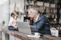 Businessman with little daughter working on laptop in cafe — Stock Photo