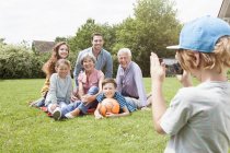 Boy taking picture of happy extended family in garden — Stock Photo