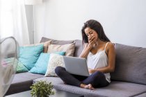 Tired teenage girl sitting on the couch with laptop — Stock Photo