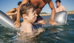 Uomini e ragazzo divertirsi con airbed in mare — Foto stock