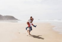 Happy mature man carrying wife piggyback on the beach — Stock Photo