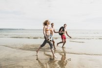 Amis marchant avec un ballon et un pneu sur la plage — Photo de stock
