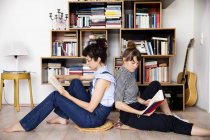 Dois amigos leitura sentado de volta para trás no chão da sala de estar — Fotografia de Stock