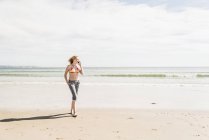 Teenage girl on cell phone walking on the beach — Stock Photo