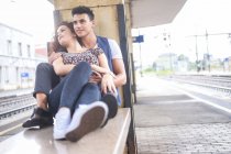 Happy young couple sitting on bench on platform — Stock Photo