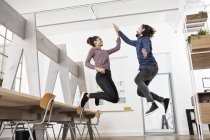 Двое счастливых коллег в офисе прыгают и дают пять — стоковое фото