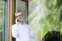Homme au téléphone debout à la porte ouverte de sa maison — Stock Photo