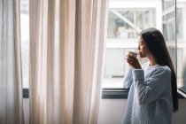 Femme avec café debout devant la fenêtre — Photo de stock