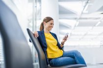 Smiling woman sitting on chair looking at cell phone — Stock Photo