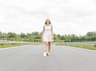 Молода жінка в білій сукні ходить босоніж по сільській дорозі — стокове фото