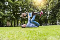 Vater hebt Tochter beim Spielen auf Wiese im Park im Gras liegend — Stockfoto