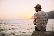 Greece, Cylcades Islands, Amorgos, man sitting at the sea at sunset — Stock Photo