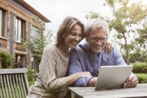 Heureux couple mature partage tablette numérique dans le jardin — Photo de stock