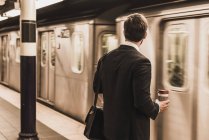 Молодой бизнесмен ждет на платформе станции метро и держит одноразовый кубок — стоковое фото