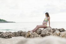 Schwangere sitzt auf Felsen am Meer — Stockfoto