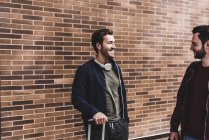 Due amici sorridenti con la borsa del carrello che parlano davanti al muro di mattoni — Foto stock