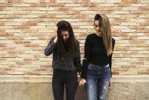 Two women holding hands in front of brick wall looking down — Stock Photo